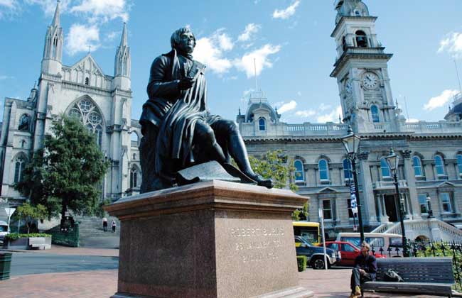 A large statue of Robert Burns in front of a grand cathedral.