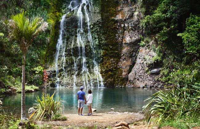 Two people standing in front of a waterfall near Haast Pass.