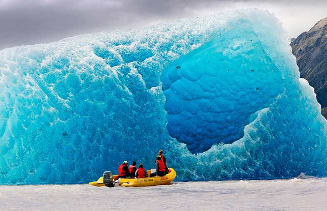 A massive, magnificent blue and icy glacier protruding from the water.