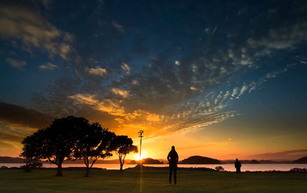 Two people heading to waters edge as the sun setts in the Bay of Islands