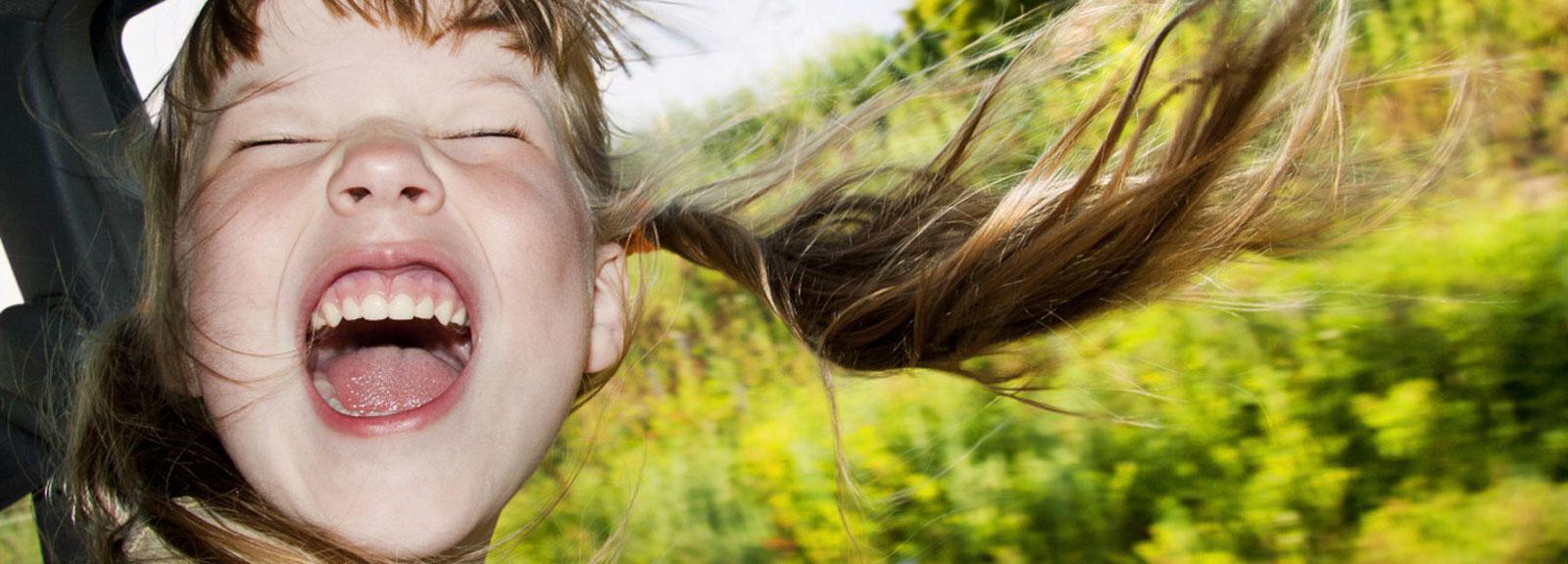 Girl screaming with joy with head out of car window gulping New Zealands fresh air.