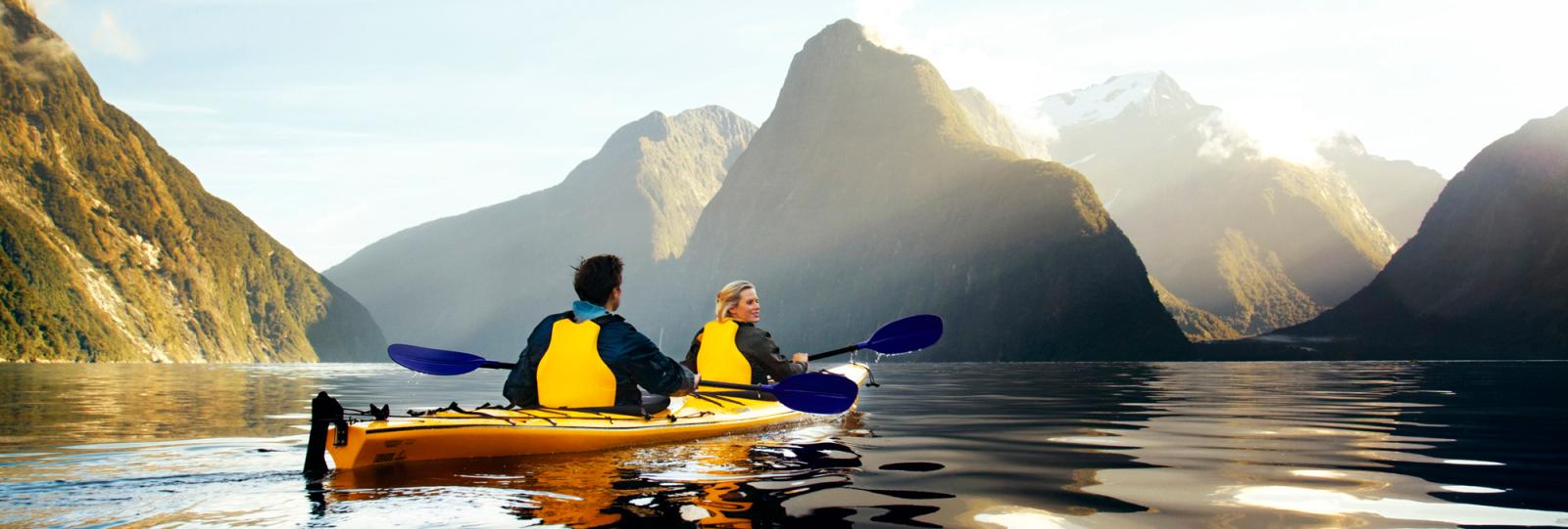 A couple kayak the length of Milford Sound, calm and sun shining.