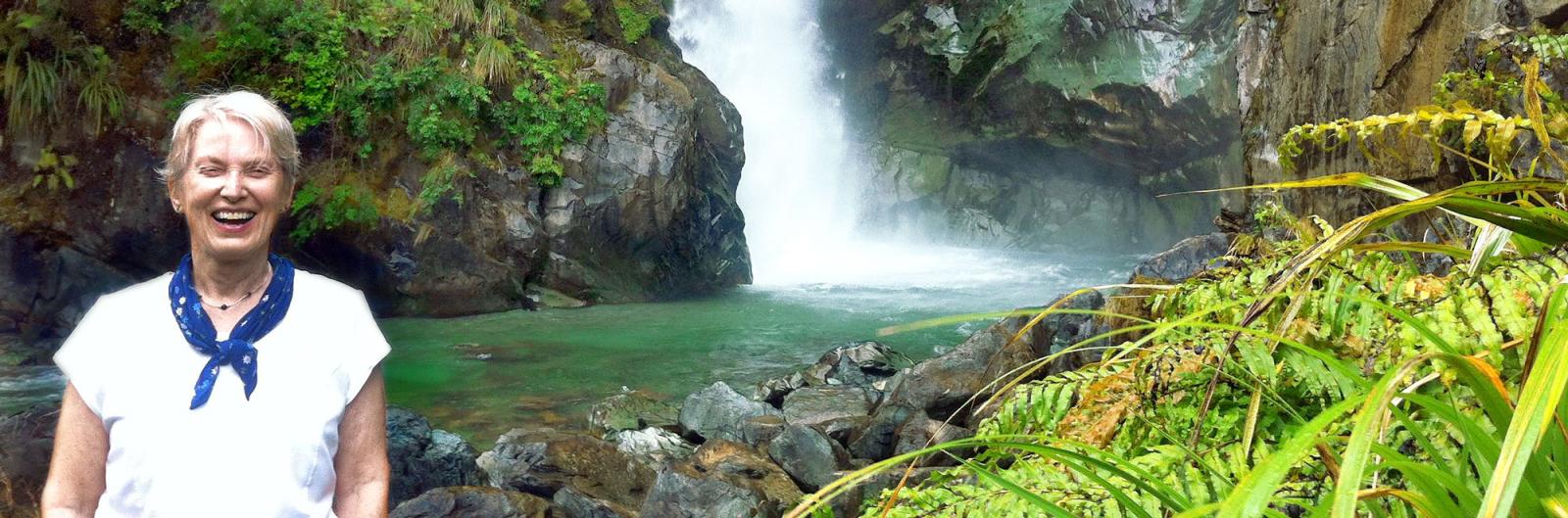 A woman standing in front of a roaring waterfall on the Hollyford Track.