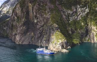Boat dwarfed by Milford Sound fjords