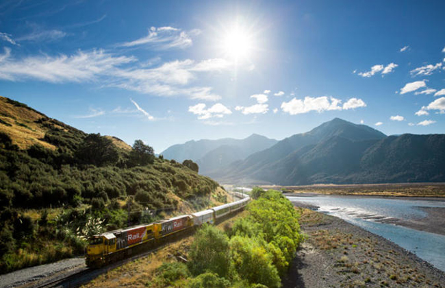 The TranzAlpine Express driving through a landscape of mountains.