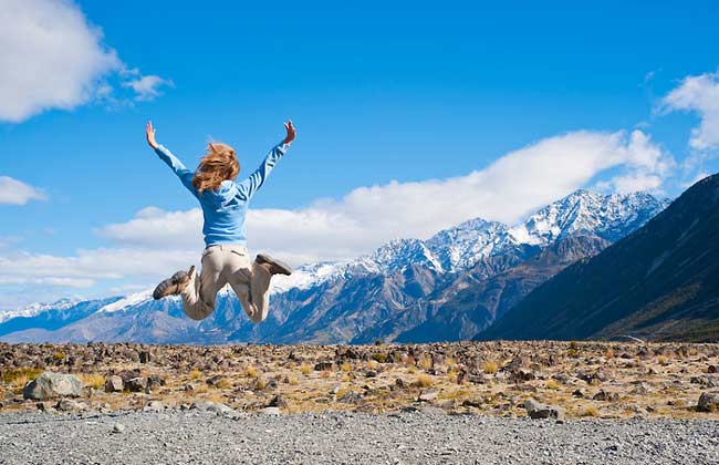 A girl jumping in the air surrounded by scenic mountains.